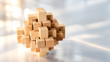 Komplexes, dreidimensionales Holzpuzzle aus ineinandergreifenden Bausteinen auf hellem Hintergrund, mit warmem Licht und sanften Schatten.